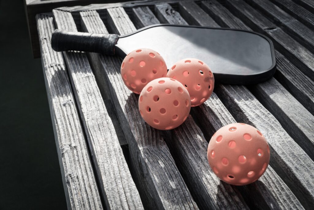 Pickleball paddle and balls on a bench.