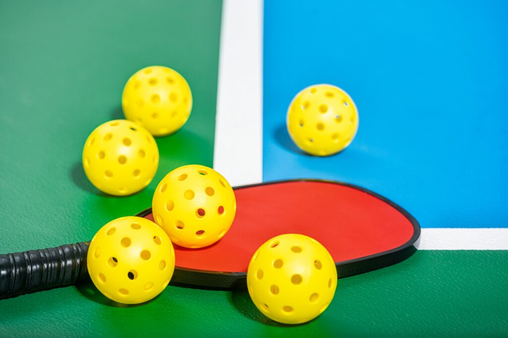 Yellow pickleballs and paddle on court.