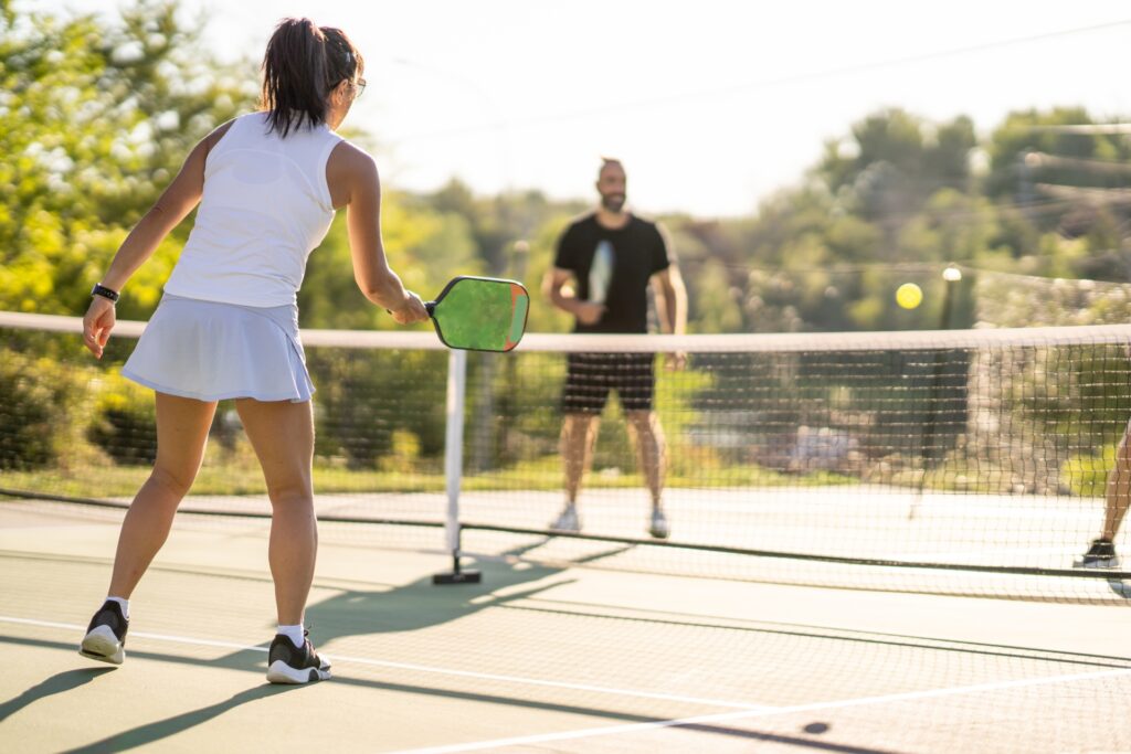 A man and woman playing pickleball outside.