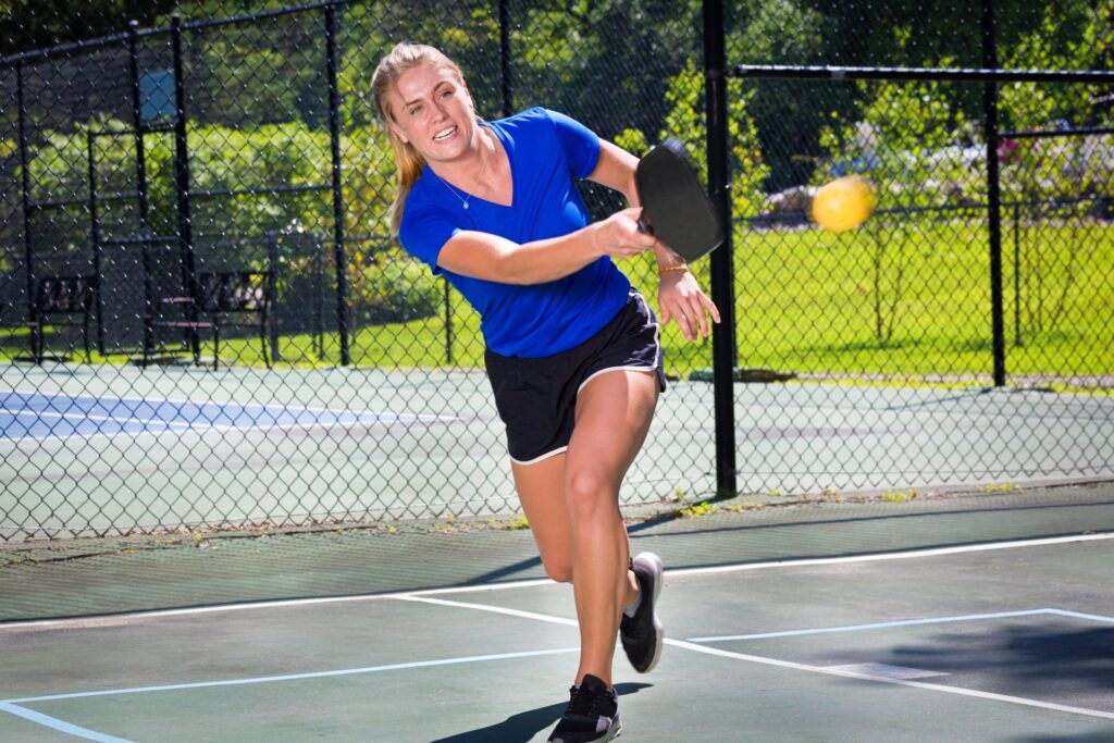 Woman in a blue shirt hitting a pickleball.