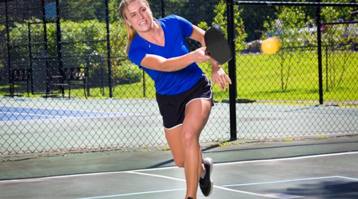 Woman in a blue shirt hitting a pickleball.